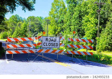 Road closed sign blocks access to rural road lined with trees Road closed sign blocks access to rural road lined with trees 142493233