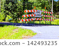 Road closed signs are set up on rural road surrounded by trees 142493235