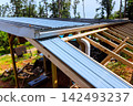 Workers install metal roofing sheets on wooden frame in rural location 142493237