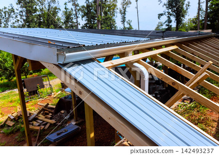 Workers install metal roofing sheets on wooden frame in rural location Workers install metal roofing sheets on wooden frame in rural location 142493237