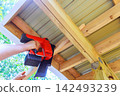 Contractor works on building project by using nail gun on wooden beams in yard 142493239