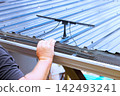 Construction worker attaches solar panel to metal roof while working outside. 142493241