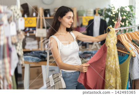 Young woman customer elect something summer clothes in store. Young woman customer elect something summer clothes in store. 142493365