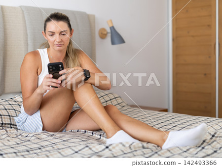 Woman scrolling phone and resting in bedroom 142493366