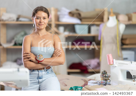 Female dressmaker sitting on table in sewing studio Female dressmaker sitting on table in sewing studio 142493367