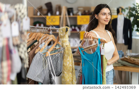 Young woman customer elect something summer clothes in store. Young woman customer elect something summer clothes in store. 142493369