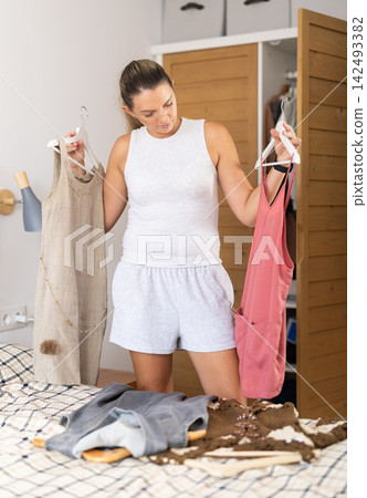 Adult woman choosing dress from wardrobe in bedroom Adult woman choosing dress from wardrobe in bedroom 142493382