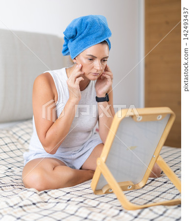 Woman in the bedroom near the mirror looking at her reflection Woman in the bedroom near the mirror looking at her reflection 142493437