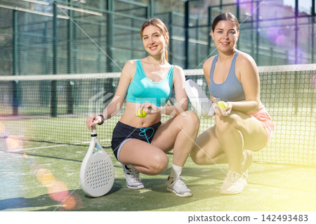 Two young sporty girls getting ready for padel game in court on sunny day Two young sporty girls getting ready for padel game in court on sunny day 142493483