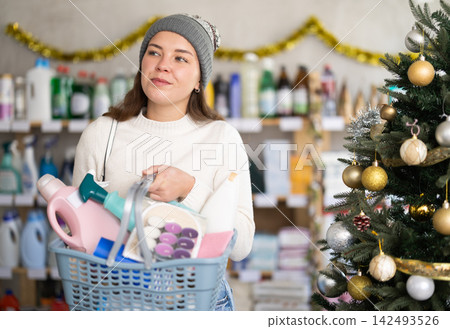 Woman with a large basket full of cleaning products on the background of a Christmas tree Woman with a large basket full of cleaning products on the background of a Christmas tree 142493526