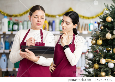 Two sellers restocking using tablet in store with New Year decoration Two sellers restocking using tablet in store with New Year decoration 142493529
