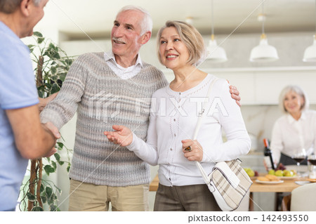 In home, mature man shake hands with couple, say hello, inviting to home family event 142493550