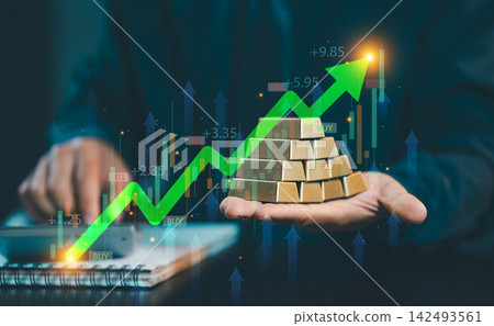Businessman holding stack of gold bullion bars with green rising stock graph and candlestick chart overlay, gold investment and wealth concept. Businessman holding stack of gold bullion bars with green rising stock graph and candlestick chart overlay, gold investment and wealth concept. 142493561