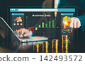 Businessman pointing at virtual business data web dashboard interface with gold coin stacks and growth chart overlay, financial analytics concept. 142493572