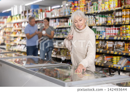 Aged female buyer looking at foods in glass display case Aged female buyer looking at foods in glass display case 142493644