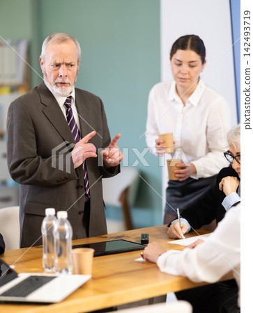 Male boss reprimanding upset subordinates sitting at table in office meeting room, expressing dissatisfaction with work Male boss reprimanding upset subordinates sitting at table in office meeting room, expressing dissatisfaction with work 142493719