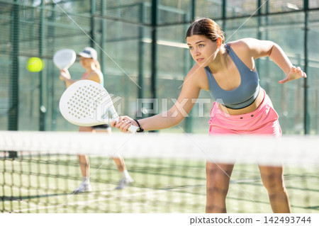 Determined sporty young woman doing her best playing padel in court Determined sporty young woman doing her best playing padel in court 142493744