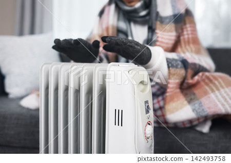 Warming hands over a heater radiator at home during a frost. This highlights a weak heating problem, freezing cold weather, and rising energy crisis costs. Warming hands over a heater radiator at home during a frost. This highlights a weak heating problem, freezing cold weather, and rising energy crisis costs. 142493758