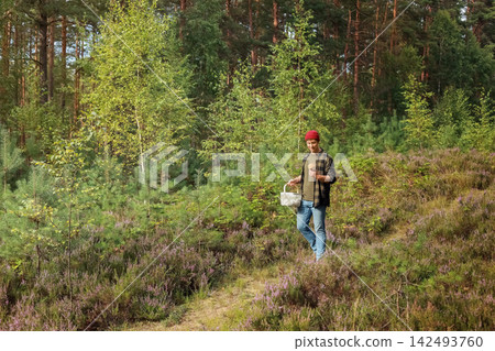 Man walking on a forest path with a basket, picking a wild mushroom. This autumn outdoor activity highlights foraging, seasonal harvest and nature connection. Man walking on a forest path with a basket, picking a wild mushroom. This autumn outdoor activity highlights foraging, seasonal harvest and nature connection. 142493760