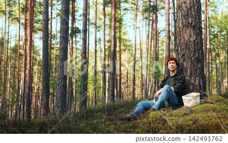 Man resting in a forest during a wild mushroom foraging trip. This outdoor activity highlights autumn harvest, mushroom picking, sustainable lifestyle and connection with nature. Man resting in a forest during a wild mushroom foraging trip. This outdoor activity highlights autumn harvest, mushroom picking, sustainable lifestyle and connection with nature. 142493762
