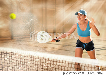Young sporty woman playing padel game in court on sunny day Young sporty woman playing padel game in court on sunny day 142493862