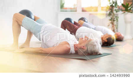 Lady does lightweight bridge pose - Setu Bandhasana and holds softball in lap. Lady does lightweight bridge pose - Setu Bandhasana and holds softball in lap. 142493990