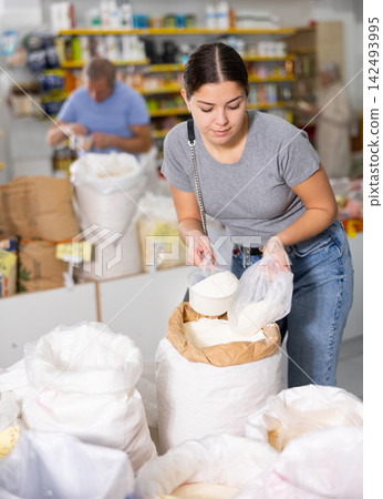 Young woman pouring wheat flour with a scoop in grocery supermarket 142493995