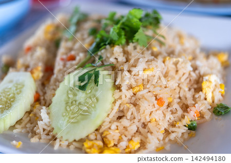 Thai egg fried rice colorful vegetables fresh cucumber cilantro served plate creating simple savory satisfying meal Thai egg fried rice colorful vegetables fresh cucumber cilantro served plate creating simple savory satisfying meal 142494180