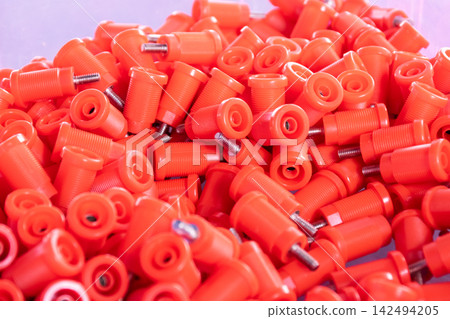 Pile of orange plastic threaded fasteners metal bolts showing industrial hardware components ready for manufacturing assembly installation Pile of orange plastic threaded fasteners metal bolts showing industrial hardware components ready for manufacturing assembly installation 142494205