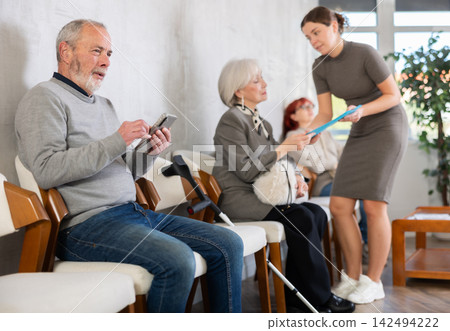 Elderly people sitting in clinic queue while social worker talks to other patients Elderly people sitting in clinic queue while social worker talks to other patients 142494222
