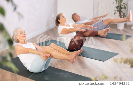 Group of elderly people doing pilates on mat in studio Group of elderly people doing pilates on mat in studio 142494231