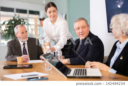 Elderly man leading meeting with senior colleagues at table Elderly man leading meeting with senior colleagues at table 142494234