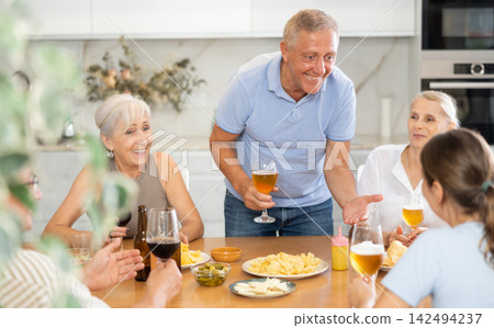 Happy carefree older man and women gathering around kitchen table Happy carefree older man and women gathering around kitchen table 142494237