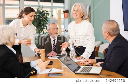 Elderly man leading meeting with senior colleagues at table Elderly man leading meeting with senior colleagues at table 142494250