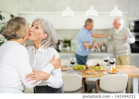 Two elderly women friends hugging in kitchen 142494251