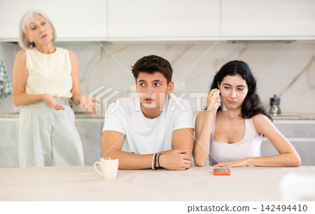 Young guy and crying girl are sitting at table and listening to their mothers swearing Young guy and crying girl are sitting at table and listening to their mothers swearing 142494410
