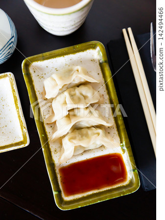 On black background stand plate with boiled gyoza dumplings served with soy sauce and chopsticks On black background stand plate with boiled gyoza dumplings served with soy sauce and chopsticks 142494466