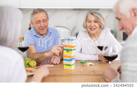Group of four mature friends is playing board game with wooden blocks in kitchen Group of four mature friends is playing board game with wooden blocks in kitchen 142494505