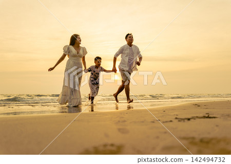 Family enjoying holiday vacation on beach at sunset, running together near ocean water while having fun during joyful seasonal trip outdoors with bright sunlight lighting landscape Family enjoying holiday vacation on beach at sunset, running together near ocean water while having fun during joyful seasonal trip outdoors with bright sunlight lighting landscape 142494732