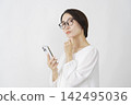 一位中年婦女在白色背景下使用智慧型手機思考。 142495036
