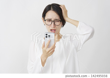 一位中年婦女雙手抱頭，在白色背景下看著她的智慧型手機。 142495038