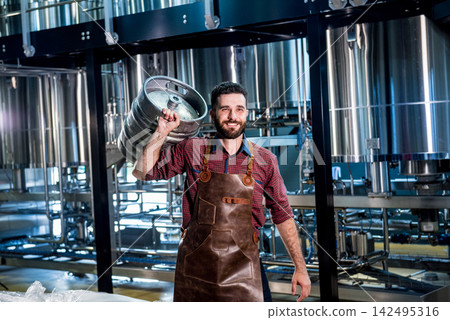 Young male brewer in leather apron holds barrel with craft beer at modern brewery factory Young male brewer in leather apron holds barrel with craft beer at modern brewery factory 142495316