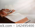 A believer's hand holding the cross of Jesus Christ above the Bible, the Word of God's life; a background for a time of spiritual meditation. 142495400