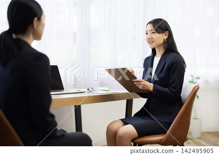 一位身著職業套裝的年輕日本女商人,面帶微笑,坐在明亮的窗邊辦公桌前做筆記,正在與客戶交談。 一位身著職業套裝的年輕日本女商人,面帶微笑,坐在明亮的窗邊辦公桌前做筆記,正在與客戶交談。 142495905