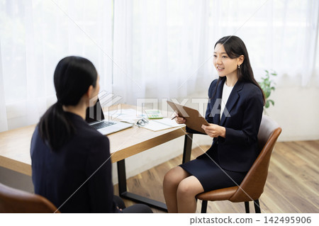 一位身著職業套裝的年輕日本女商人,面帶微笑,坐在明亮的窗邊辦公桌前做筆記,正在與客戶交談。 一位身著職業套裝的年輕日本女商人,面帶微笑,坐在明亮的窗邊辦公桌前做筆記,正在與客戶交談。 142495906