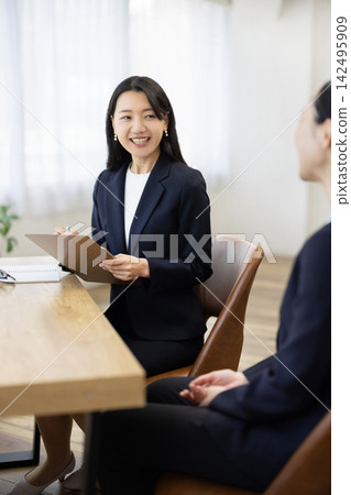 一位身著職業套裝的年輕日本女商人,面帶微笑,坐在明亮的窗邊辦公桌前做筆記,正在與客戶交談。 一位身著職業套裝的年輕日本女商人,面帶微笑,坐在明亮的窗邊辦公桌前做筆記,正在與客戶交談。 142495909
