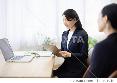一位身著職業套裝的年輕日本女商人,面帶微笑,坐在明亮的窗邊辦公桌前做筆記,正在與客戶交談。 一位身著職業套裝的年輕日本女商人,面帶微笑,坐在明亮的窗邊辦公桌前做筆記,正在與客戶交談。 142495910