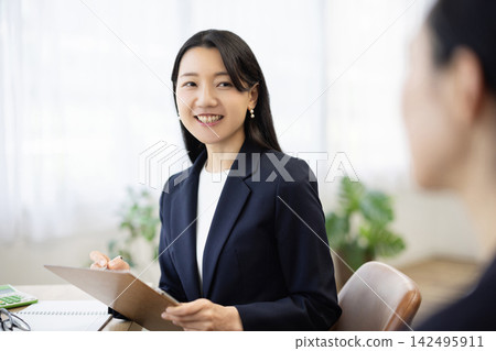 一位身著職業套裝的年輕日本女商人,面帶微笑,坐在明亮的窗邊辦公桌前做筆記,正在與客戶交談。 一位身著職業套裝的年輕日本女商人,面帶微笑,坐在明亮的窗邊辦公桌前做筆記,正在與客戶交談。 142495911