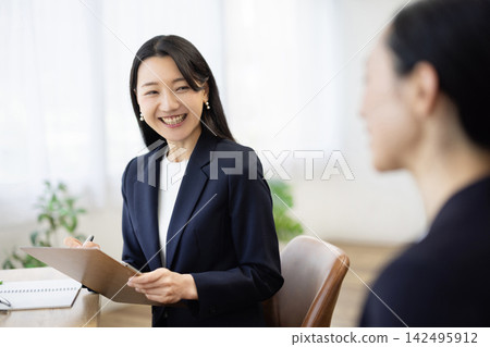 一位身著職業套裝的年輕日本女商人,面帶微笑,坐在明亮的窗邊辦公桌前做筆記,正在與客戶交談。 一位身著職業套裝的年輕日本女商人,面帶微笑,坐在明亮的窗邊辦公桌前做筆記,正在與客戶交談。 142495912