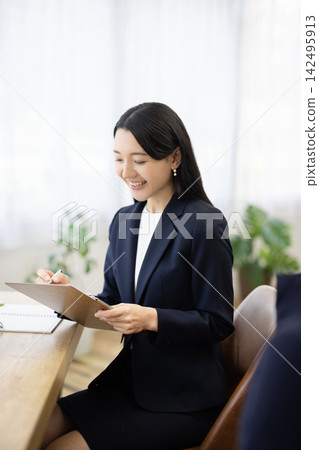 一位身著職業套裝的年輕日本女商人,面帶微笑,坐在明亮的窗邊辦公桌前做筆記,正在與客戶交談。 一位身著職業套裝的年輕日本女商人,面帶微笑,坐在明亮的窗邊辦公桌前做筆記,正在與客戶交談。 142495913